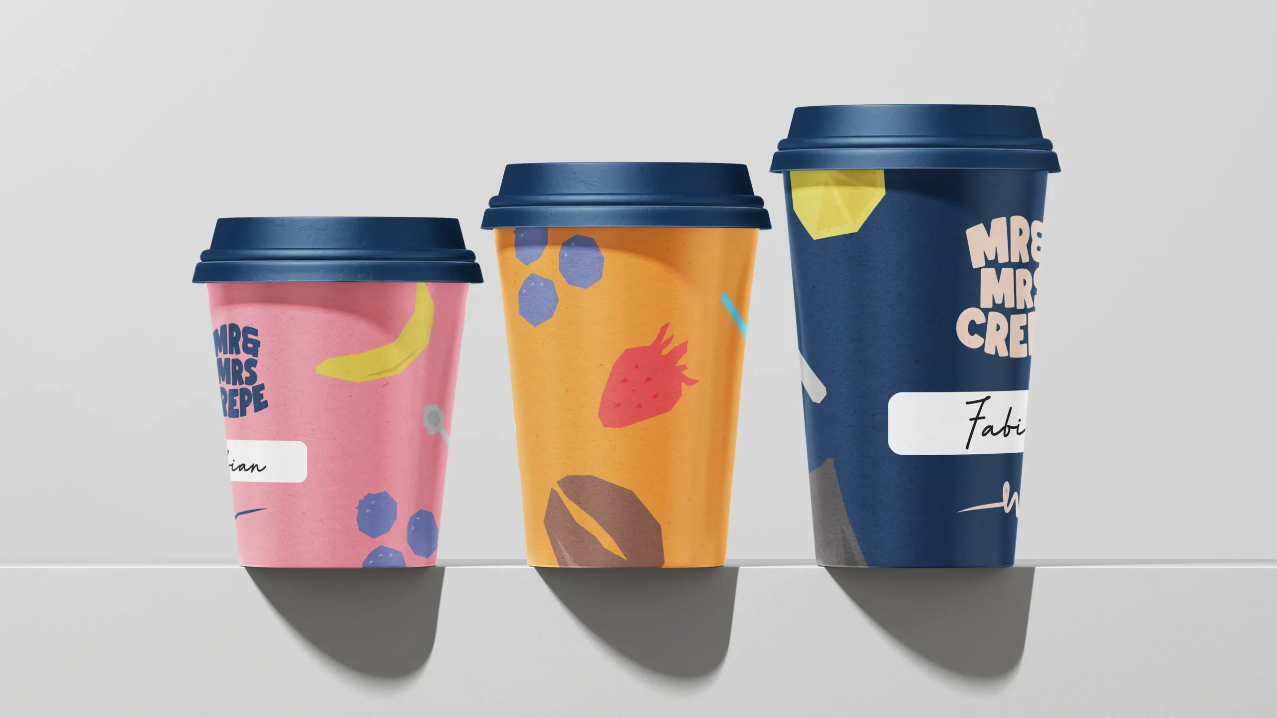 MrandMrsCrepe_Showcase_007 Three Mr & Mrs Crepe branded coffee cups of varying sizes with illustrations and dark blue lids.
